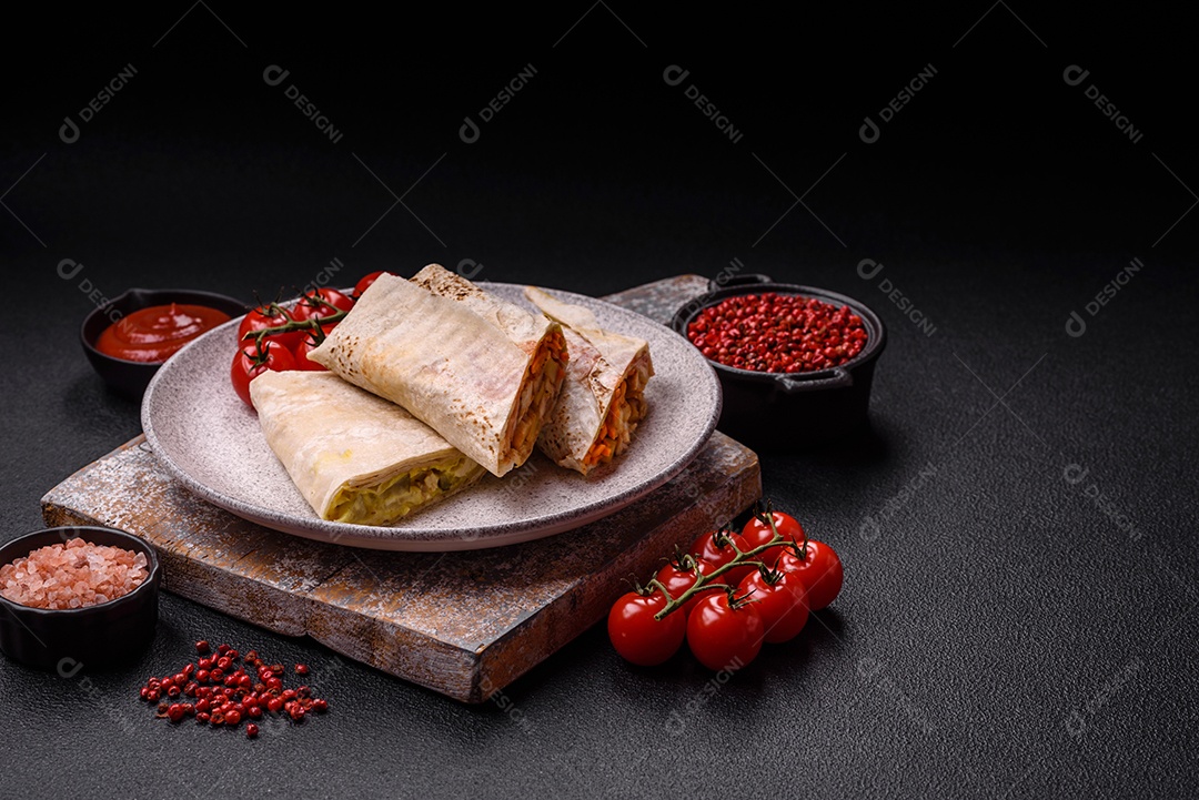 Delicioso rolo suculento ou shawarma com frango, tomate, salada e molho sobre um fundo escuro de concreto