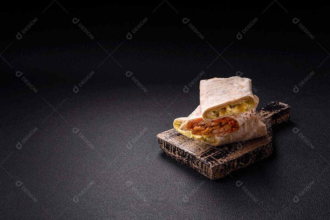 Delicioso rolo suculento ou shawarma com frango, tomate, salada e molho sobre um fundo escuro de concreto