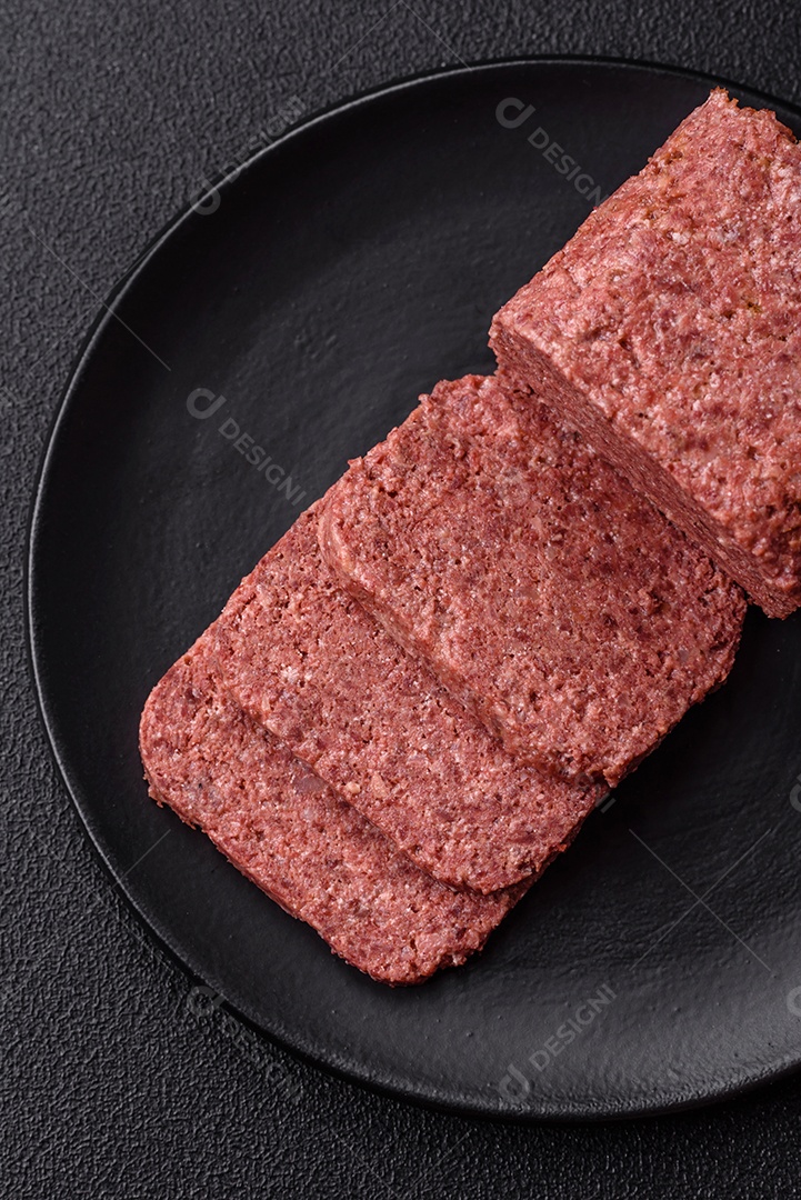 Delicioso presunto rosa enlatado com sal, especiarias e ervas sobre um fundo escuro de concreto