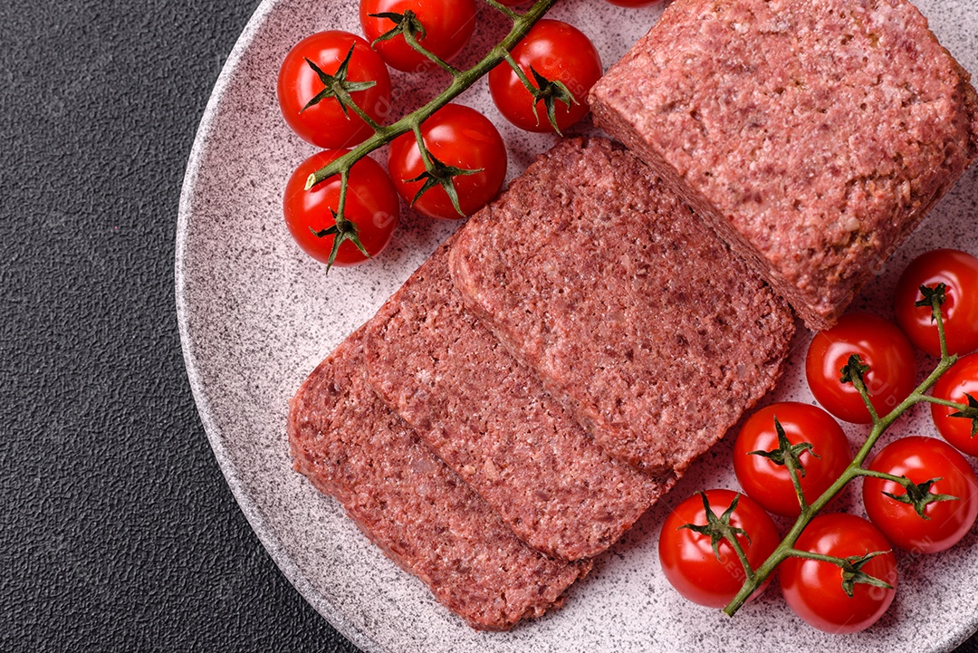 Delicioso presunto rosa enlatado com sal, especiarias e ervas sobre um fundo escuro de concreto