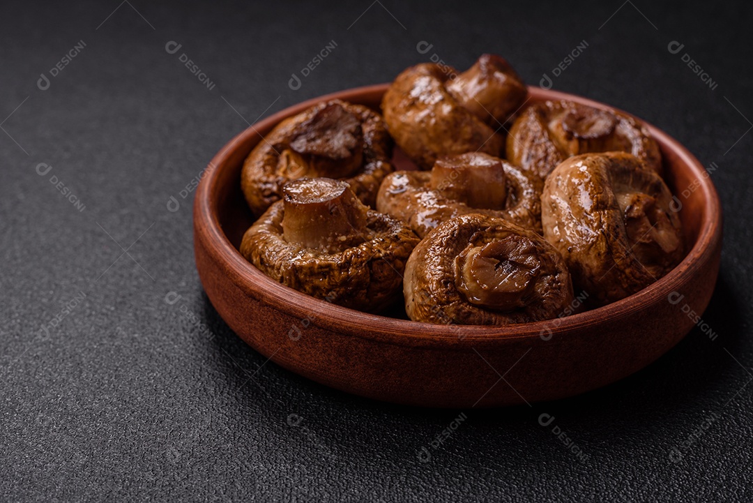 Deliciosos champignons inteiros e suculentos assados ​​na grelha com sal e especiarias em uma placa de cerâmica sobre um fundo escuro de concreto