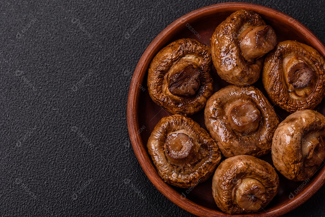 Deliciosos champignons inteiros e suculentos assados ​​na grelha com sal e especiarias em uma placa de cerâmica sobre um fundo escuro de concreto