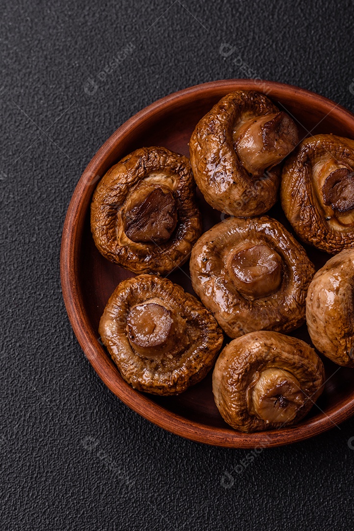 Deliciosos champignons inteiros e suculentos assados ​​na grelha com sal e especiarias em uma placa de cerâmica sobre um fundo escuro de concreto