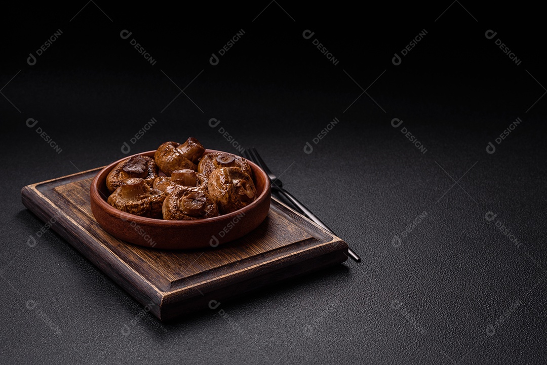 Deliciosos champignons inteiros e suculentos assados ​​na grelha com sal e especiarias em uma placa de cerâmica sobre um fundo escuro de concreto