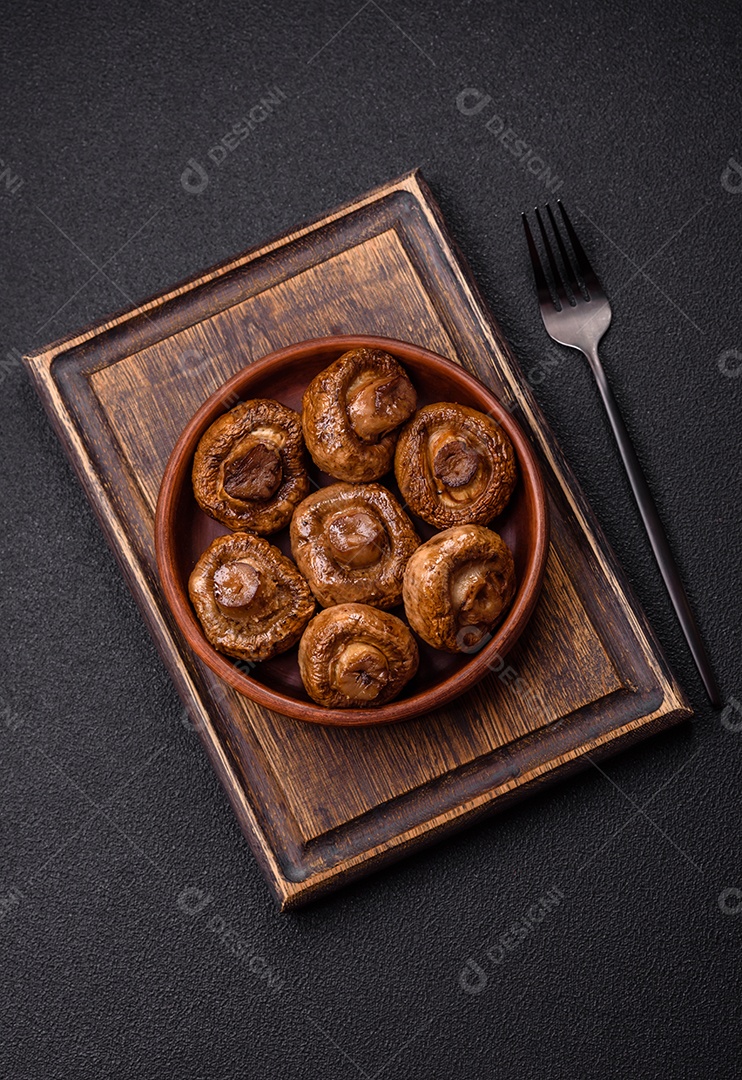 Deliciosos champignons inteiros e suculentos assados ​​na grelha com sal e especiarias em uma placa de cerâmica sobre um fundo escuro de concreto
