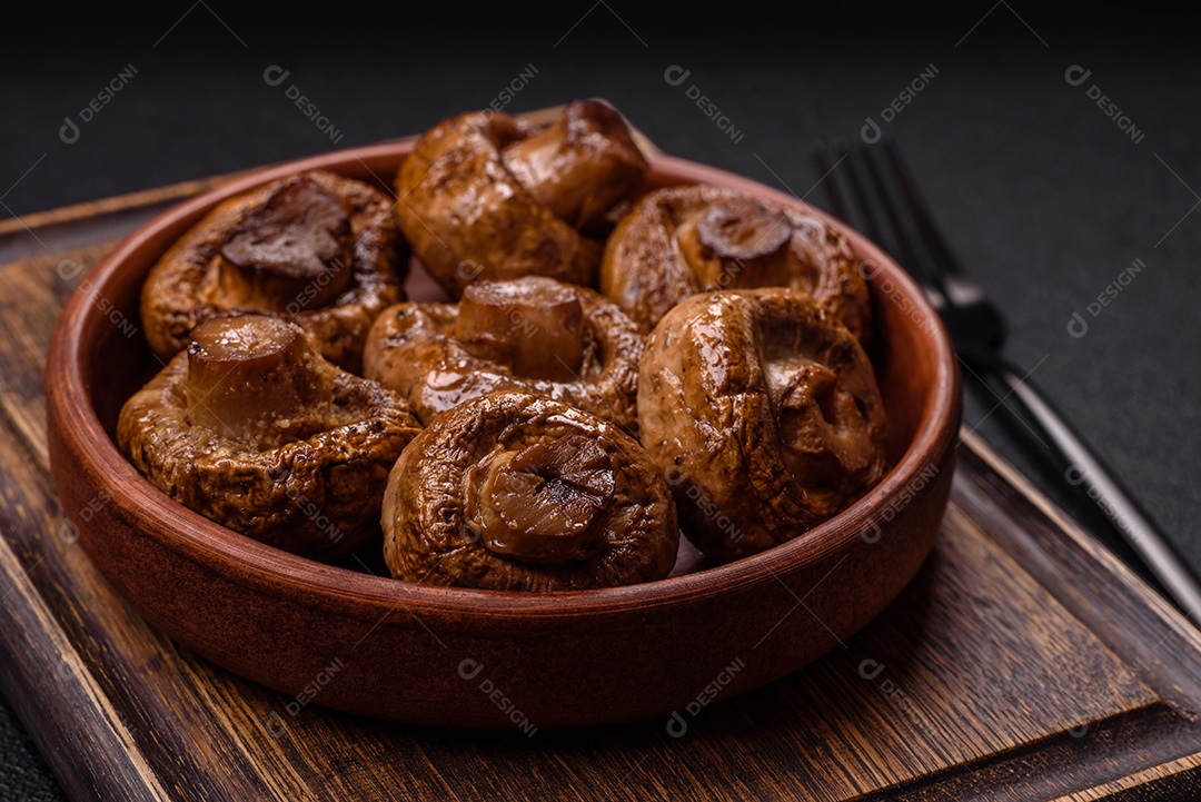 Deliciosos champignons inteiros e suculentos assados ​​na grelha com sal e especiarias em uma placa de cerâmica sobre um fundo escuro de concreto