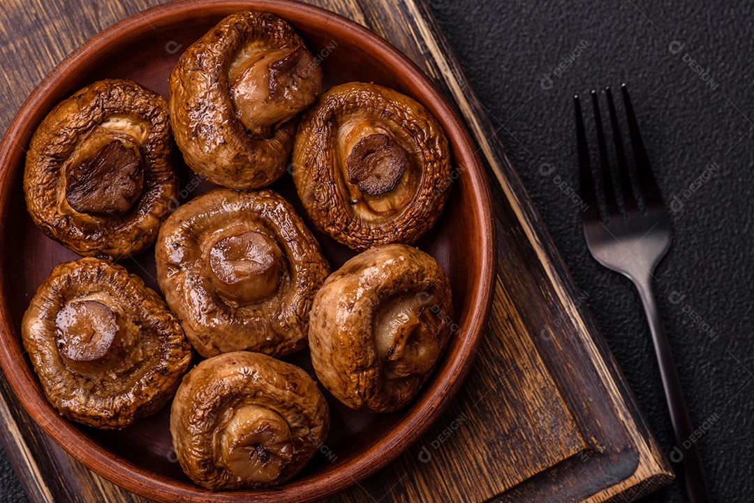 Deliciosos champignons inteiros e suculentos assados ​​na grelha com sal e especiarias em uma placa de cerâmica sobre um fundo escuro de concreto