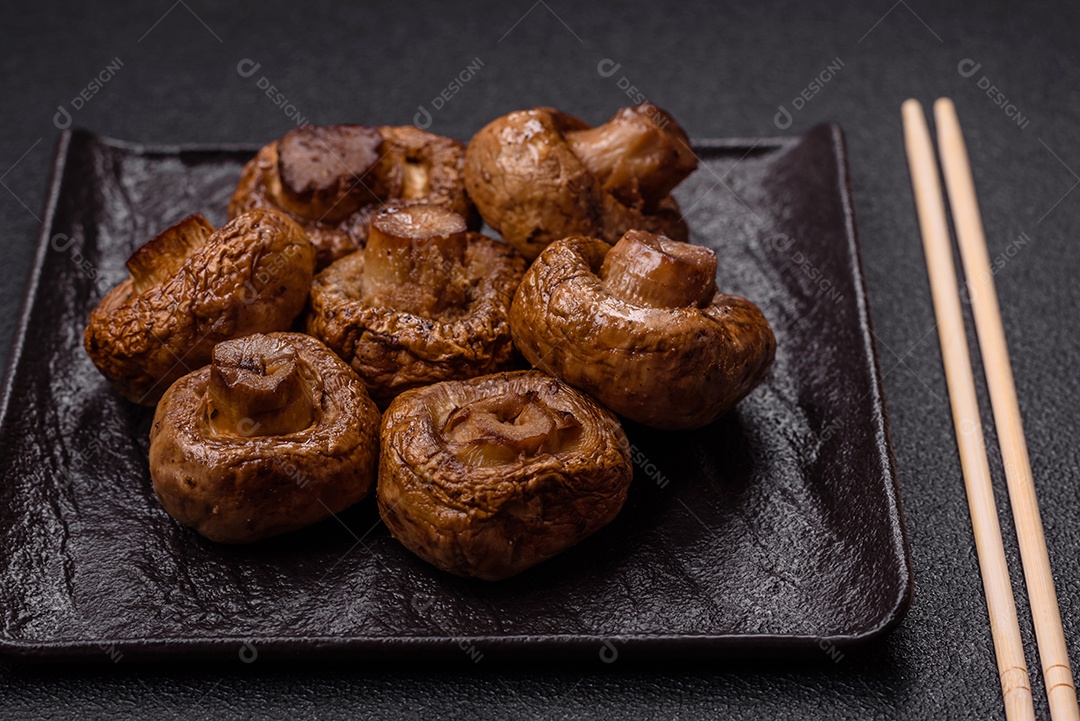 Deliciosos champignons inteiros e suculentos assados ​​na grelha com sal e especiarias em uma placa de cerâmica sobre um fundo escuro de concret