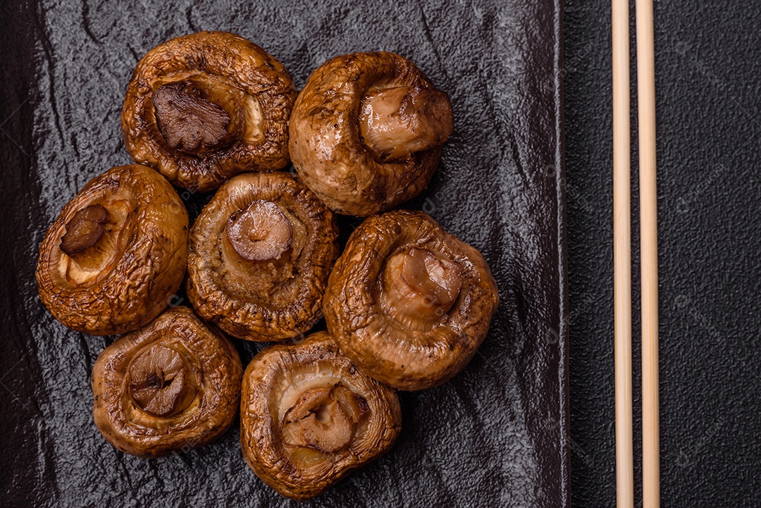 Deliciosos champignons inteiros e suculentos assados ​​na grelha com sal e especiarias em uma placa de cerâmica sobre um fundo escuro de concreto