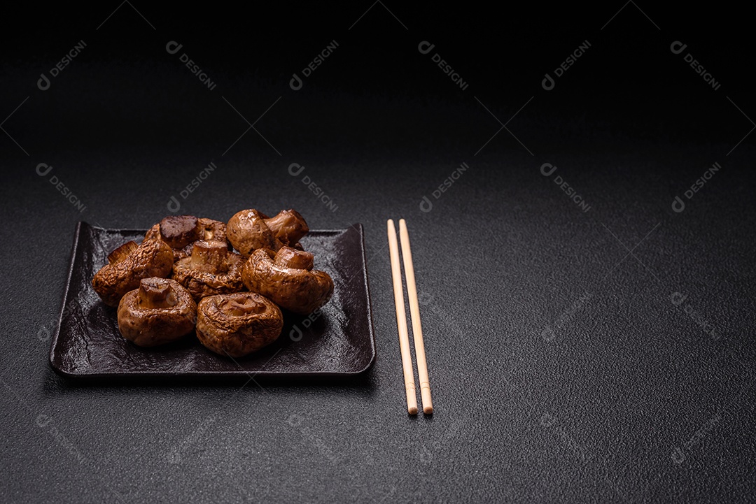 Deliciosos champignons inteiros e suculentos assados ​​na grelha com sal e especiarias em uma placa de cerâmica sobre um fundo escuro de concreto