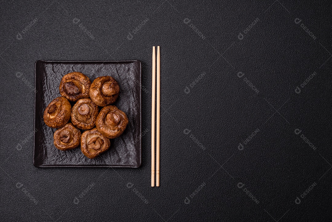 Deliciosos champignons inteiros e suculentos assados ​​na grelha com sal e especiarias em uma placa de cerâmica sobre um fundo escuro de concreto