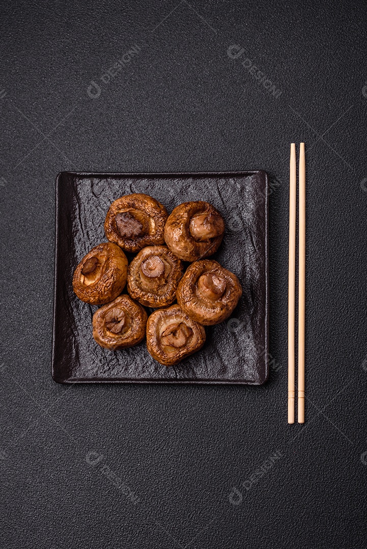 Deliciosos champignons inteiros e suculentos assados ​​na grelha com sal e especiarias em uma placa de cerâmica sobre um fundo escuro de concreto