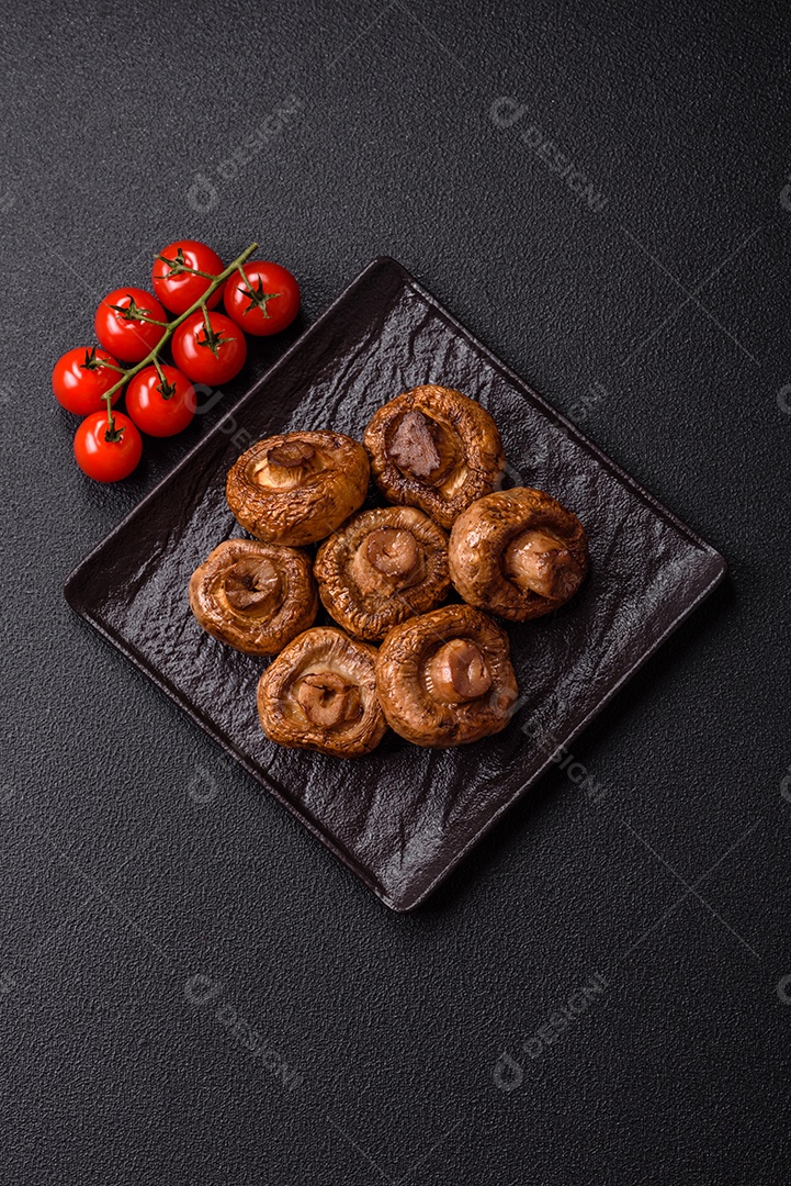 Deliciosos champignons inteiros e suculentos assados ​​na grelha com sal e especiarias em uma placa de cerâmica sobre um fundo escuro de concreto