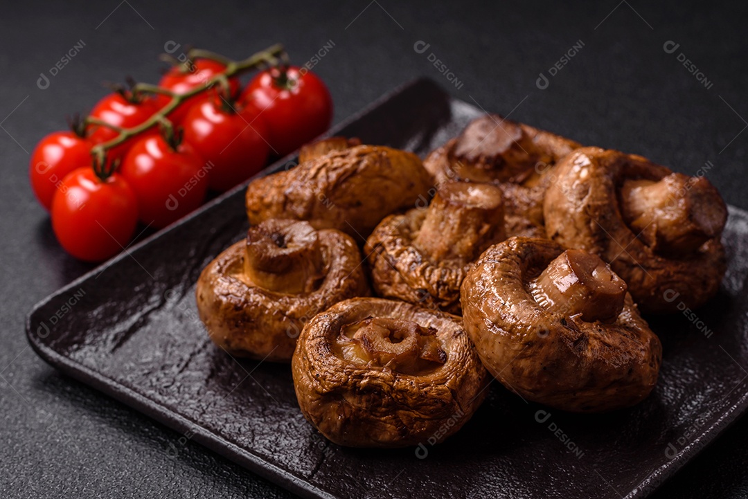 Deliciosos champignons inteiros e suculentos assados ​​na grelha com sal e especiarias em uma placa de cerâmica sobre um fundo escuro de concreto