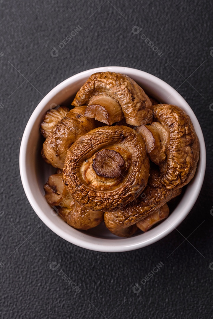 Deliciosos champignons inteiros e suculentos assados ​​na grelha com sal e especiarias em uma placa de cerâmica sobre um fundo escuro de concreto
