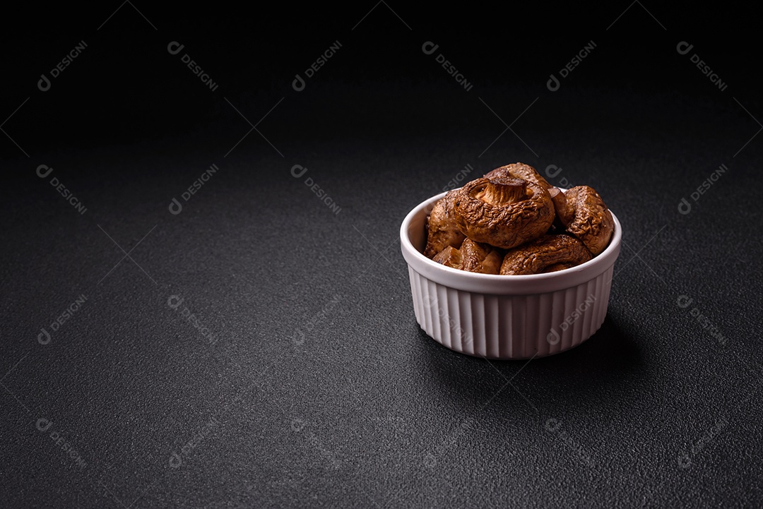 Deliciosos champignons inteiros e suculentos assados ​​na grelha com sal e especiarias em uma placa de cerâmica sobre um fundo escuro de concreto