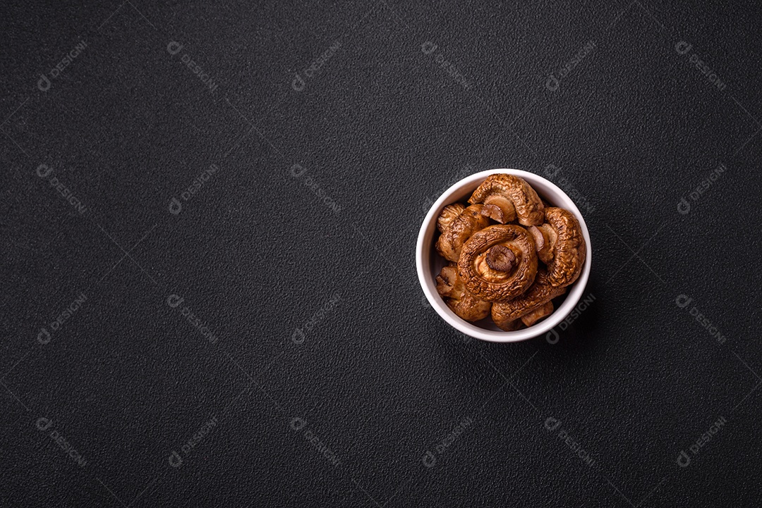 Deliciosos champignons inteiros e suculentos assados ​​na grelha com sal e especiarias em uma placa de cerâmica sobre um fundo escuro de concreto