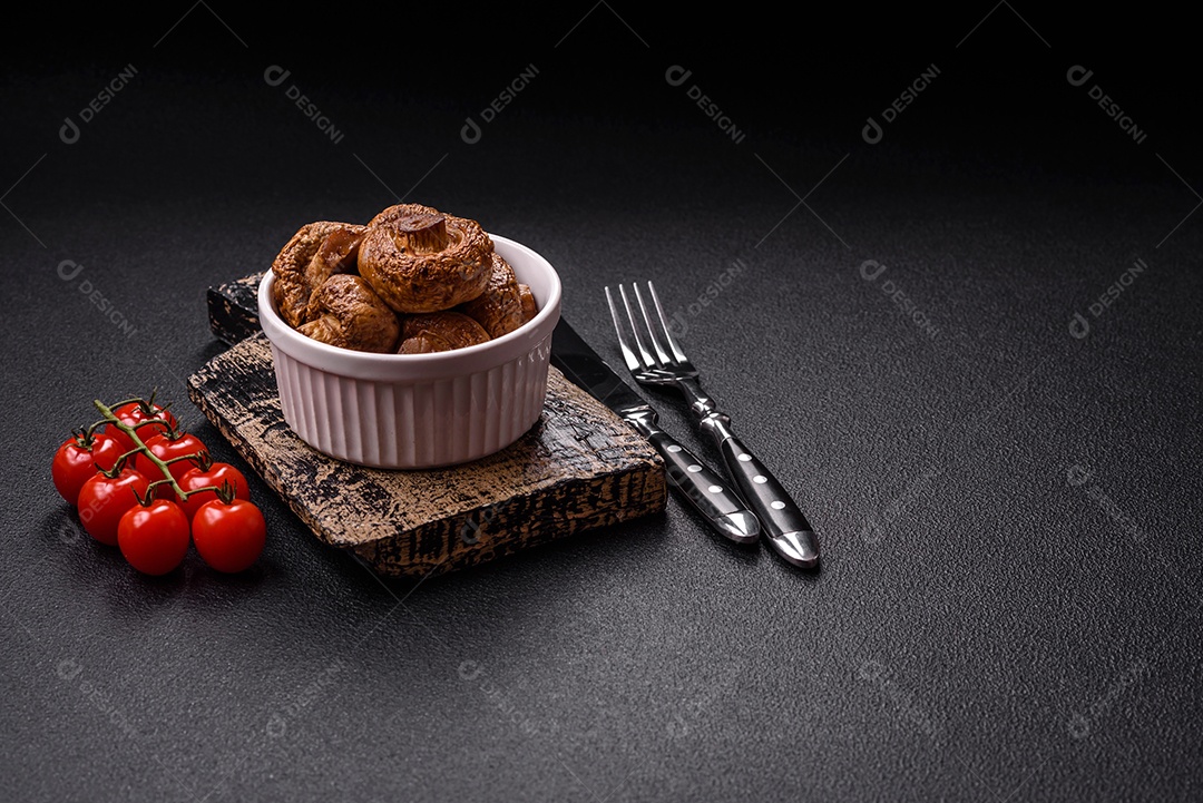 Deliciosos champignons inteiros e suculentos assados ​​na grelha com sal e especiarias em uma placa de cerâmica sobre um fundo escuro de concreto