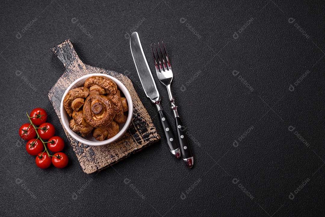 Deliciosos champignons inteiros e suculentos assados ​​na grelha com sal e especiarias em uma placa de cerâmica sobre um fundo escuro de concreto