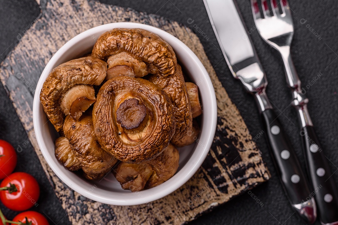 Deliciosos champignons inteiros e suculentos assados ​​na grelha com sal e especiarias em uma placa de cerâmica sobre um fundo escuro de concreto