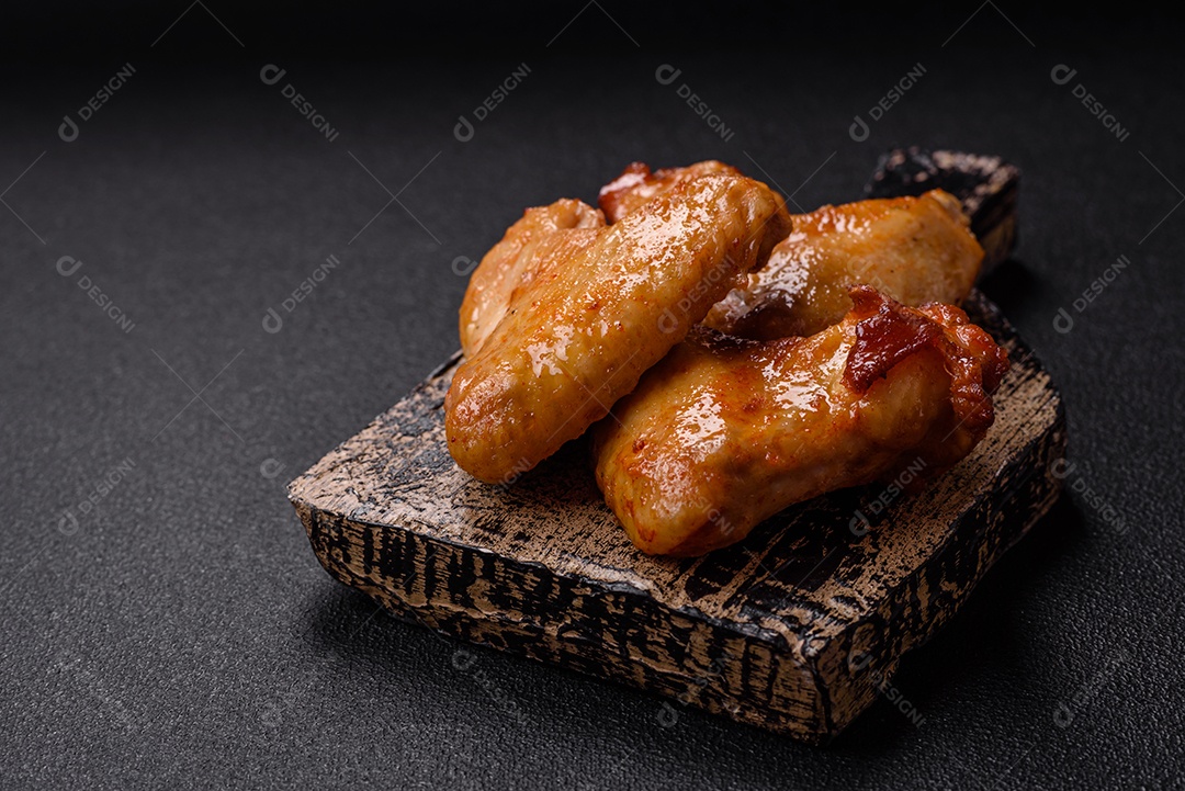 Deliciosas asas de frango frito com sal, especiarias e ervas sobre um fundo escuro de concreto