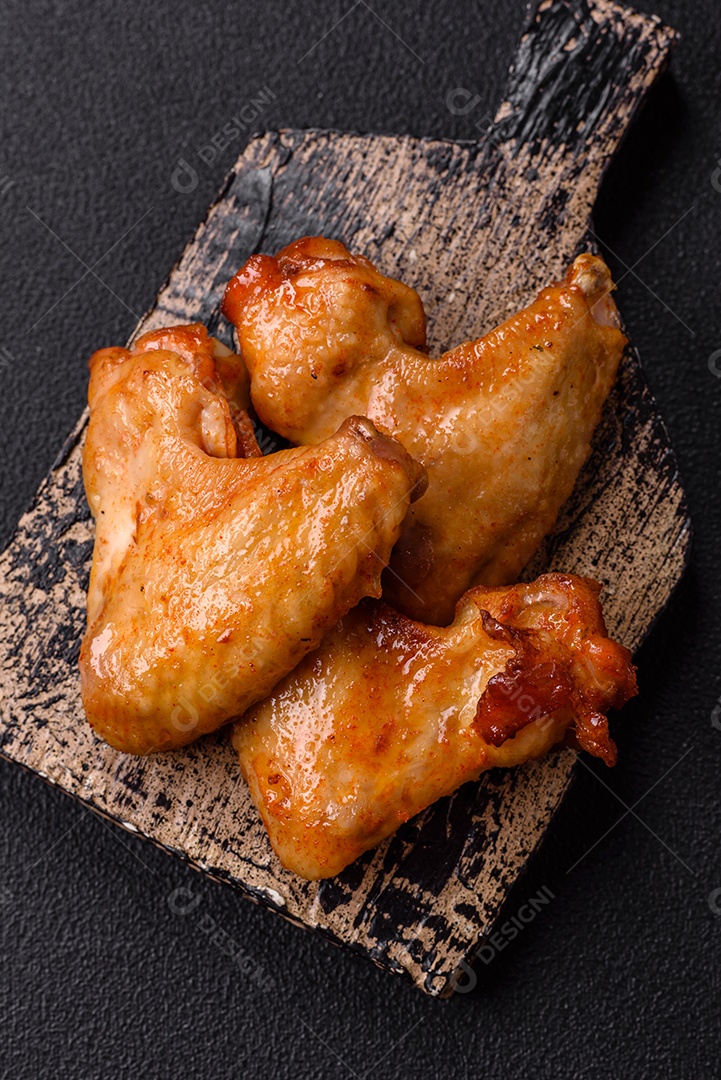 Deliciosas asas de frango frito com sal, especiarias e ervas sobre um fundo escuro de concreto
