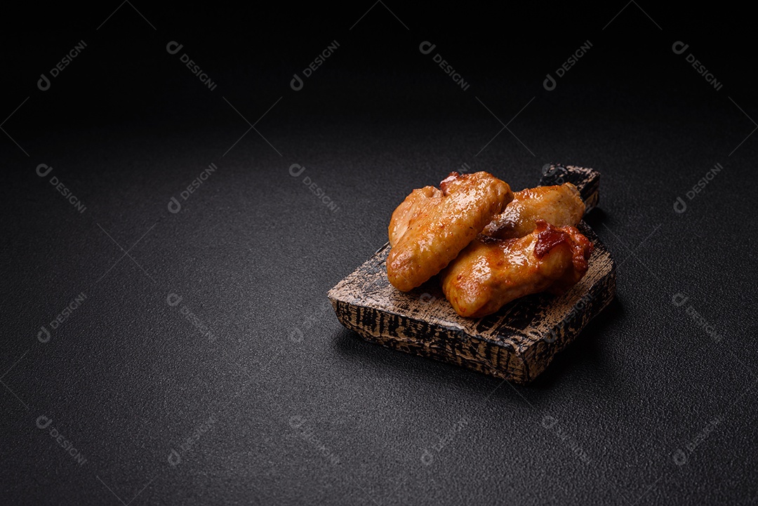 Deliciosas asas de frango frito com sal, especiarias e ervas sobre um fundo escuro de concret