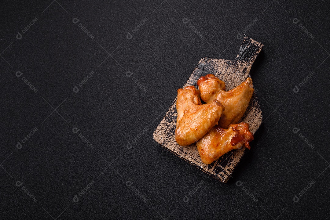 Deliciosas asas de frango frito com sal, especiarias e ervas sobre um fundo escuro de concreto