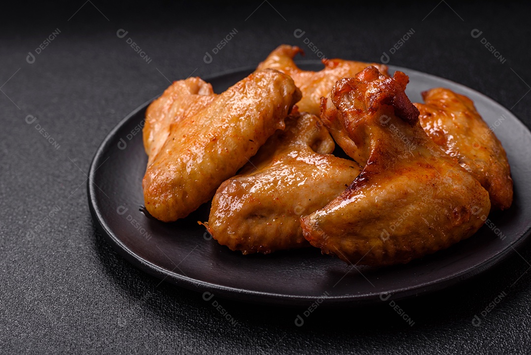 Deliciosas asas de frango frito com sal, especiarias e ervas sobre um fundo escuro de concreto