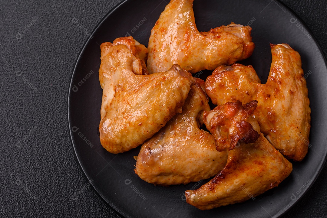 Deliciosas asas de frango frito com sal, especiarias e ervas sobre um fundo escuro de concreto