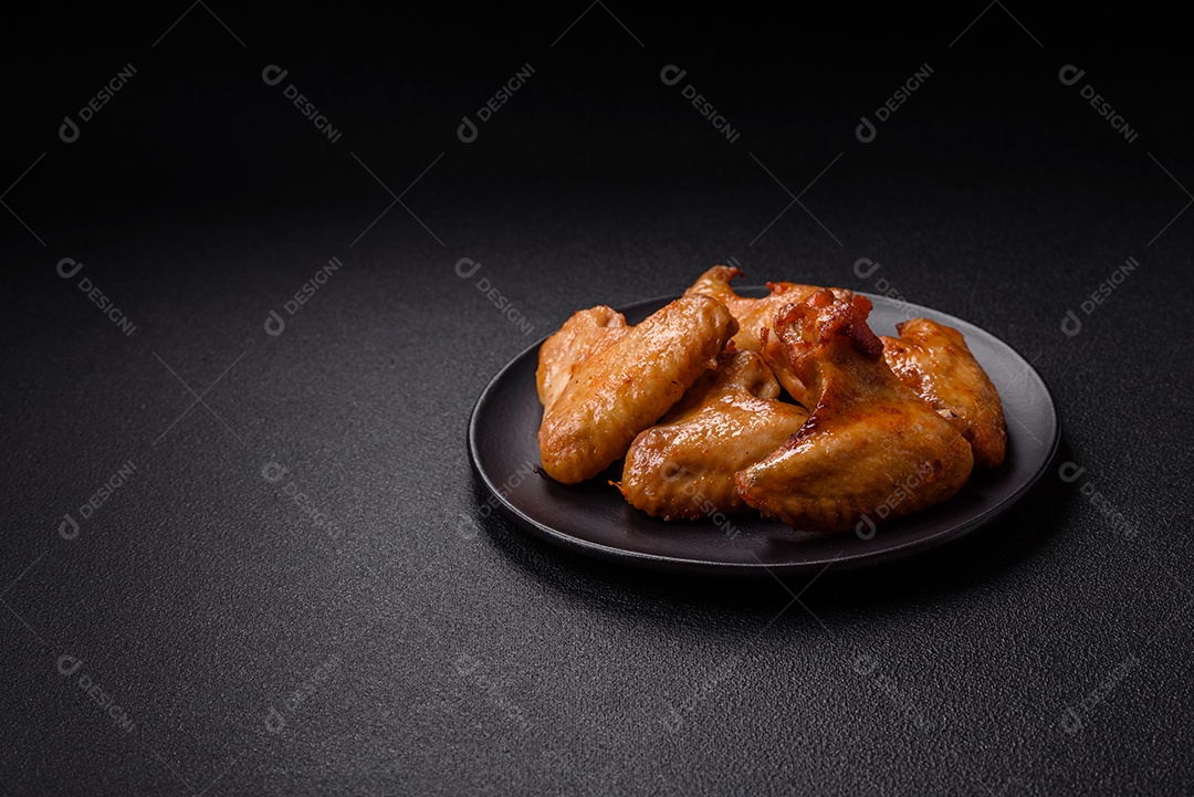 Deliciosas asas de frango frito com sal, especiarias e ervas sobre um fundo escuro de concreto