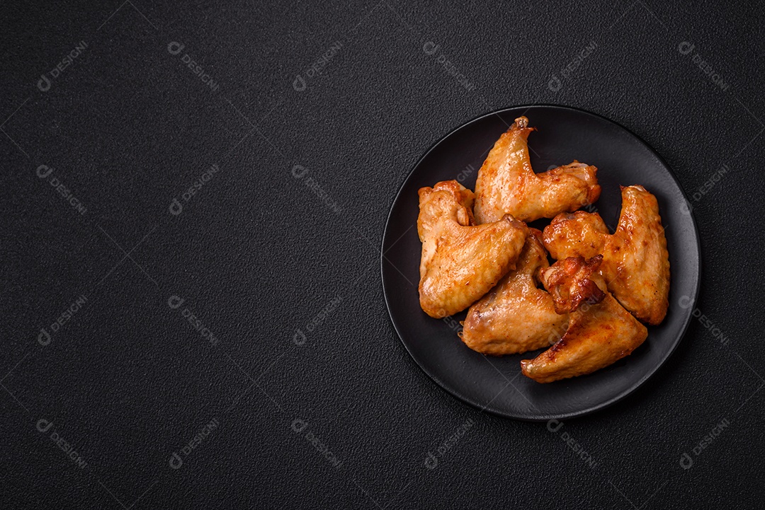 Deliciosas asas de frango frito com sal, especiarias e ervas sobre um fundo escuro de concreto