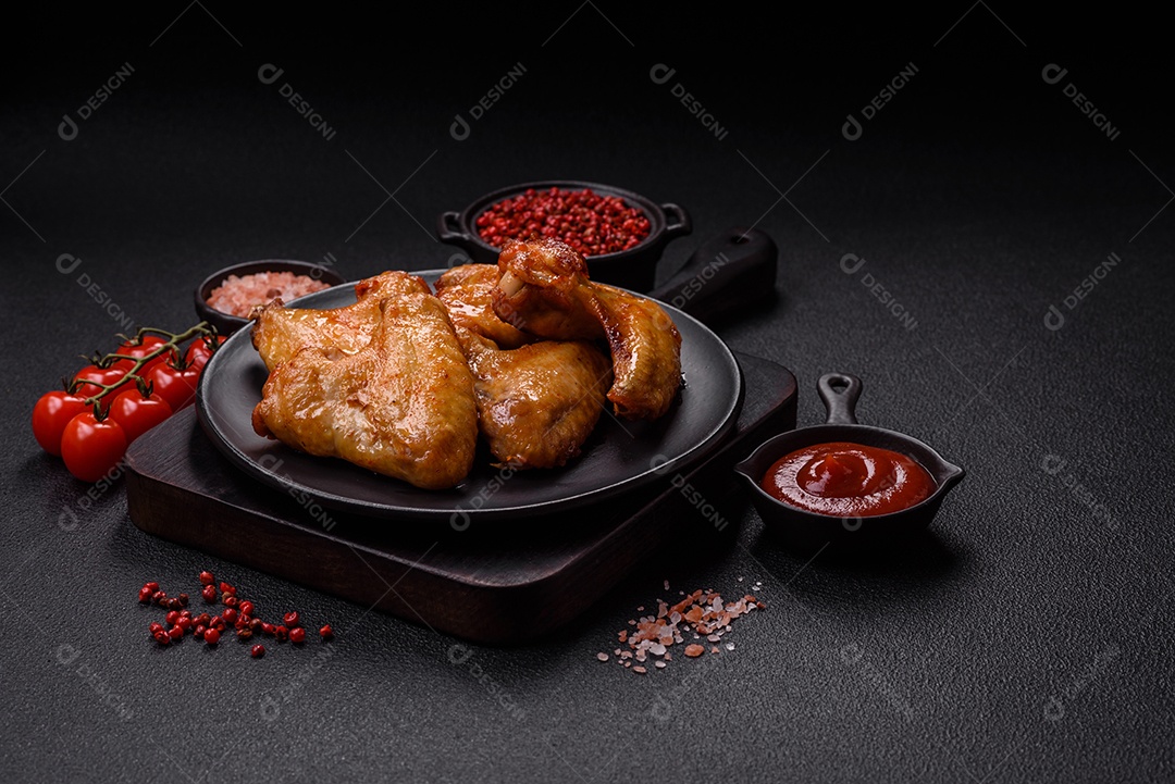 Deliciosas asas de frango frito com sal, especiarias e ervas sobre um fundo escuro de concreto