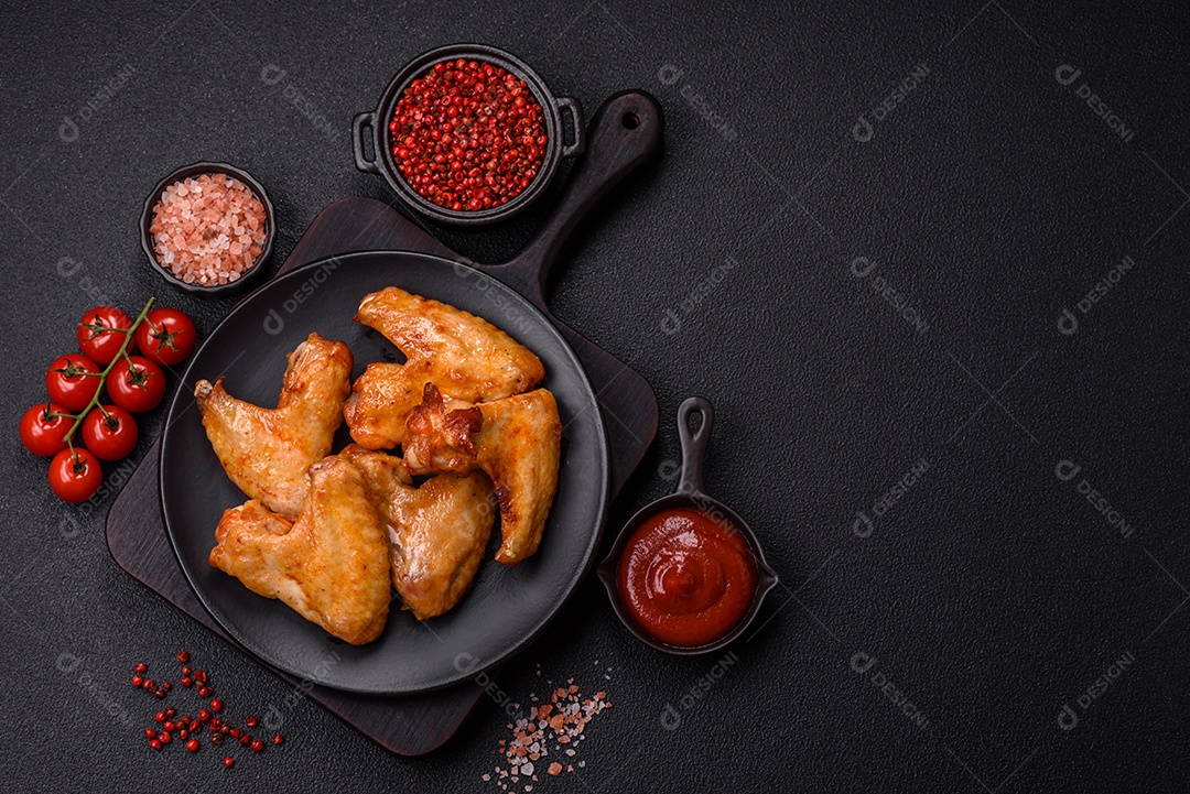 Deliciosas asas de frango frito com sal, especiarias e ervas sobre um fundo escuro de concreto