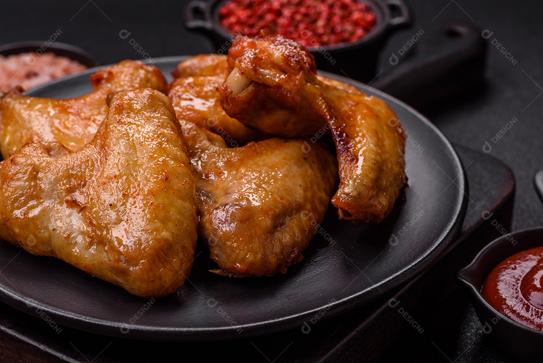 Deliciosas asas de frango frito com sal, especiarias e ervas sobre um fundo escuro de concreto