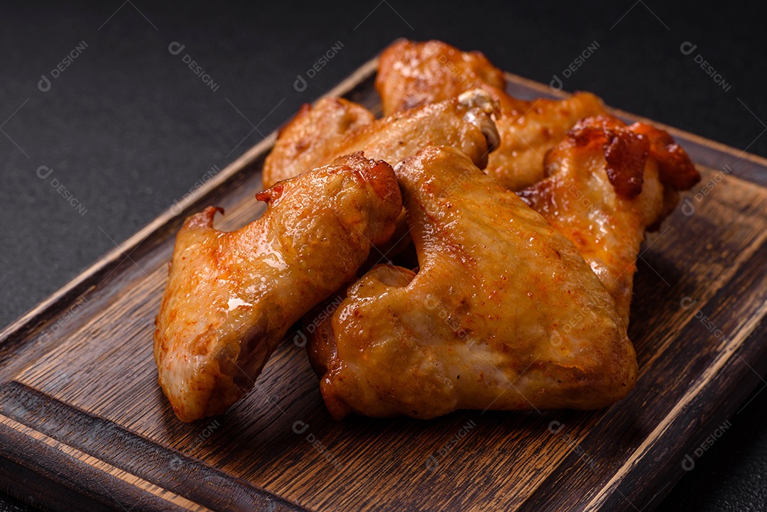 Deliciosas asas de frango frito com sal, especiarias e ervas sobre um fundo escuro de concreto