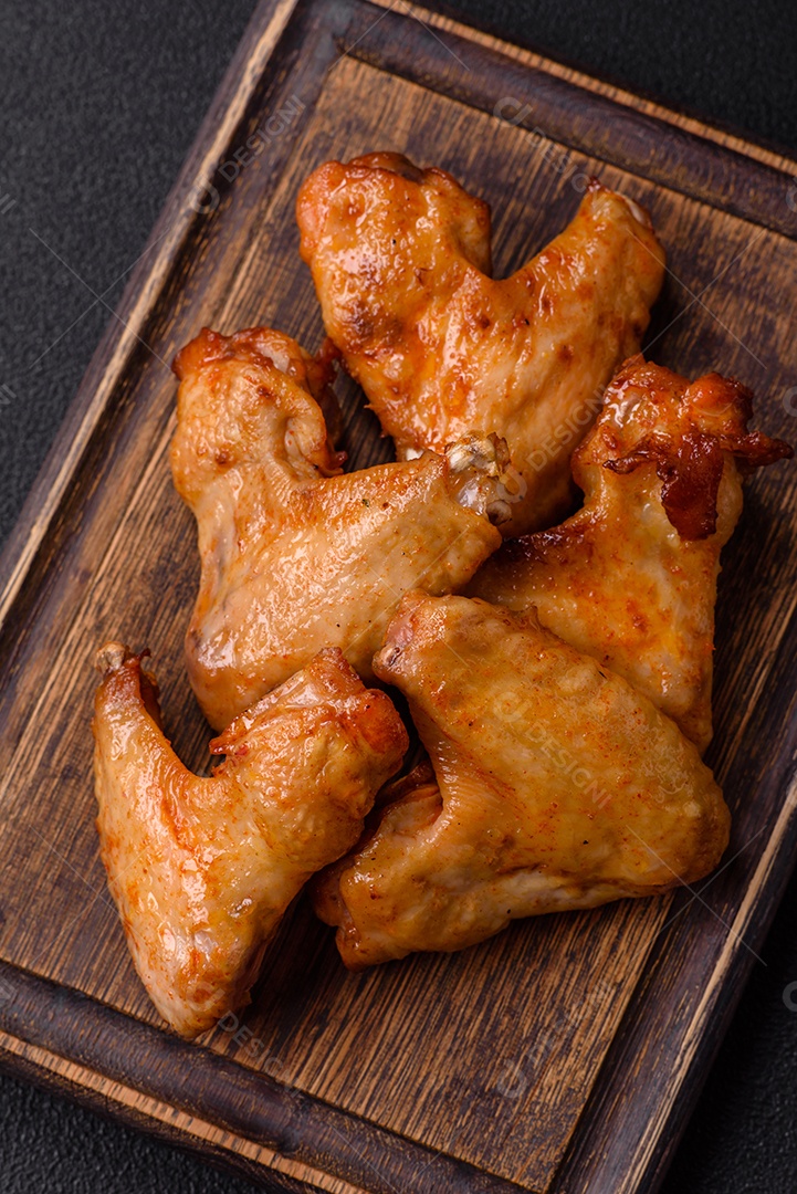 Deliciosas asas de frango frito com sal, especiarias e ervas sobre um fundo escuro de concreto