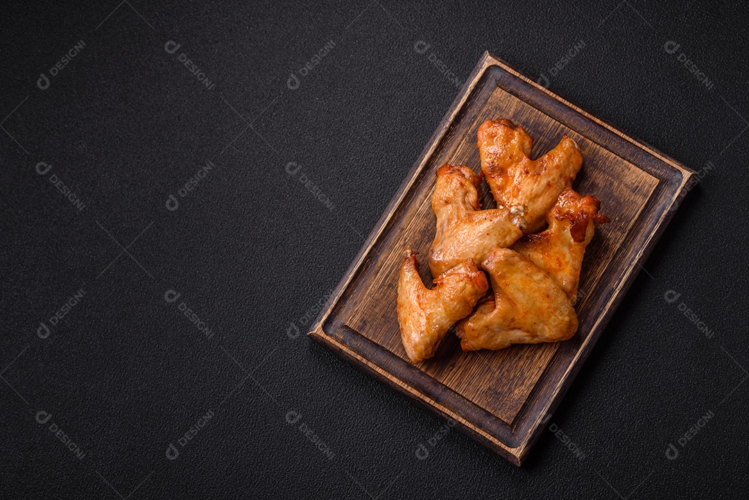Deliciosas asas de frango frito com sal, especiarias e ervas sobre um fundo escuro de concreto
