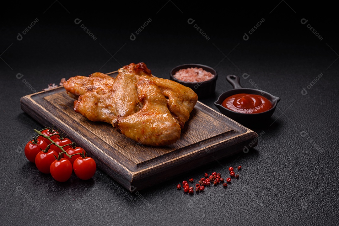 Deliciosas asas de frango frito com sal, especiarias e ervas sobre um fundo escuro de concreto