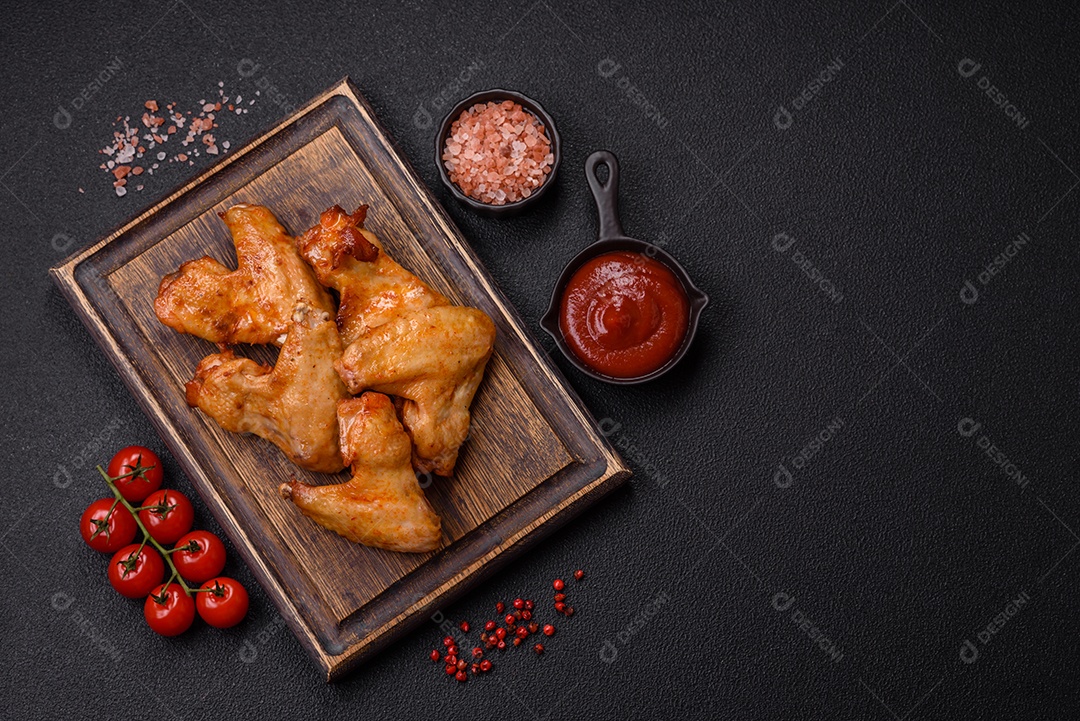 Deliciosas asas de frango frito com sal, especiarias e ervas sobre um fundo escuro de concreto