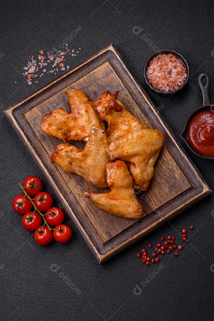 Deliciosas asas de frango frito com sal, especiarias e ervas sobre um fundo escuro de concreto