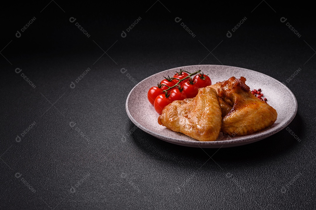 Deliciosas asas de frango frito com sal, especiarias e ervas sobre um fundo escuro de concreto