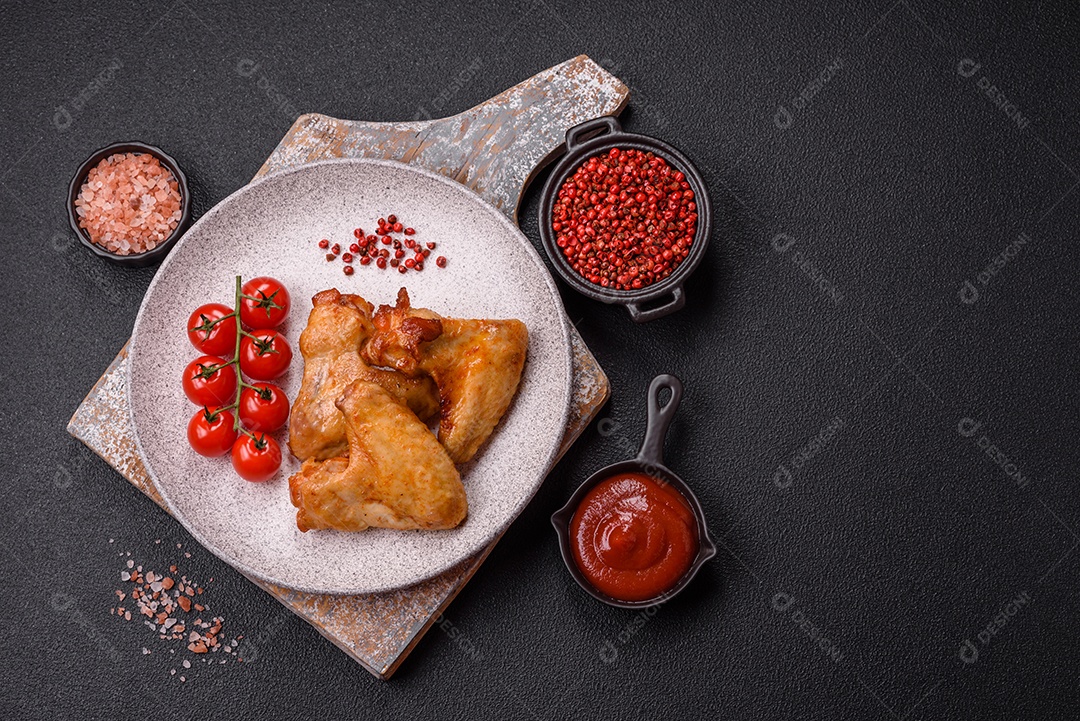 Deliciosas asas de frango frito com sal, especiarias e ervas sobre um fundo escuro de concreto