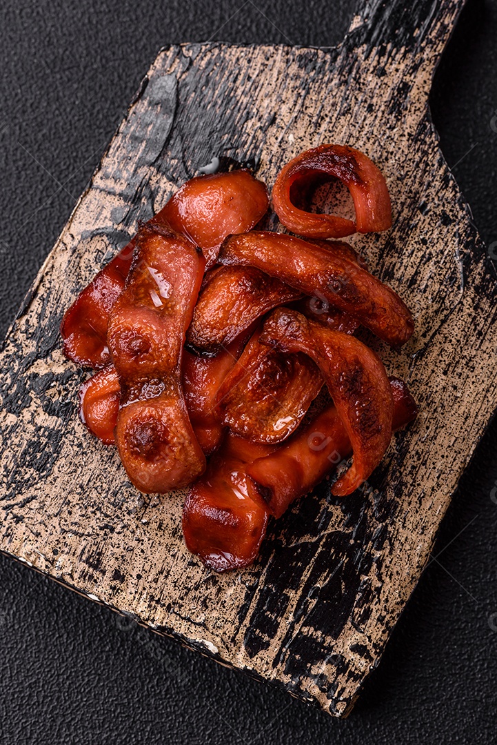 Salsichas fritas cortadas com sal e especiarias como ingrediente para um café da manhã inglês sobre fundo escuro de concreto