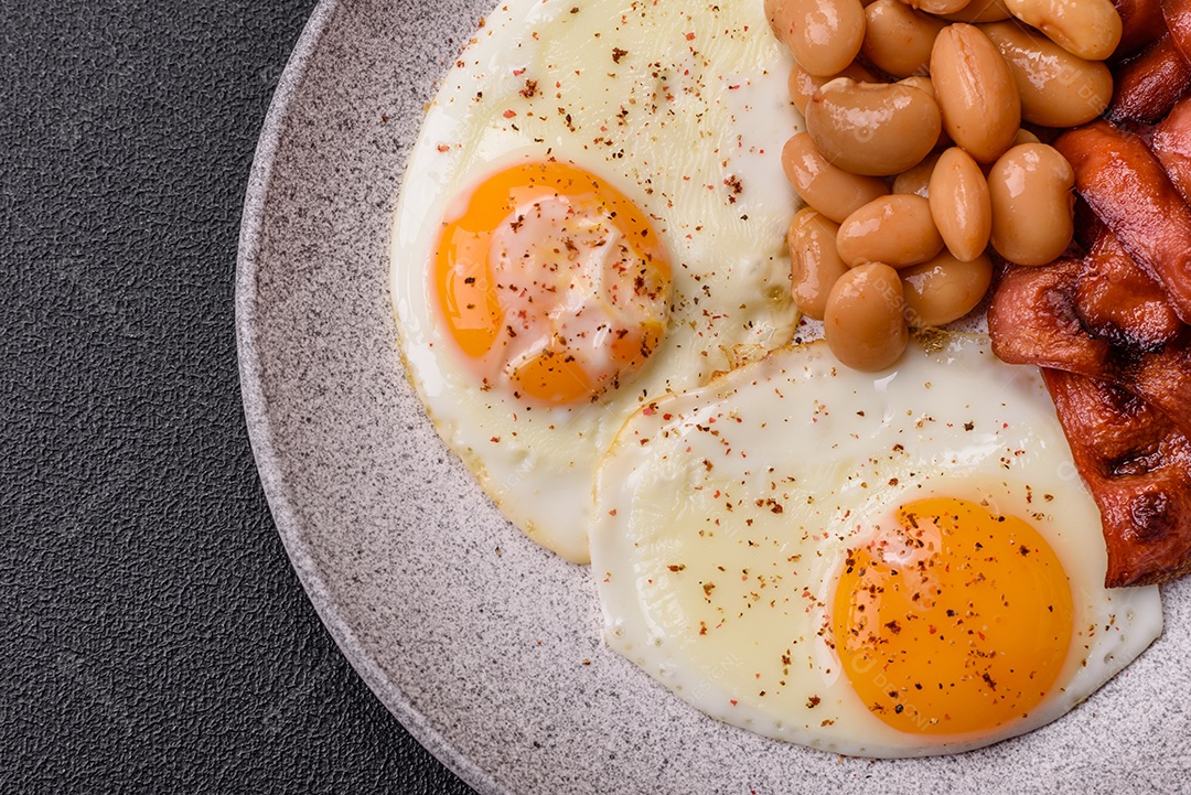 Café da manhã inglês com ovos fritos, bacon, feijão, tomate, especiarias e ervas. Um início de dia saudável e nutritivo