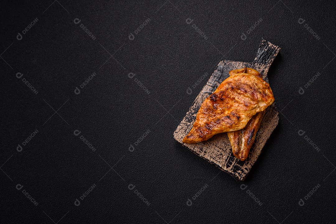 Delicioso filé de frango grelhado fresco com especiarias e ervas em um fundo escuro de concreto. Um prato cozido no fogo