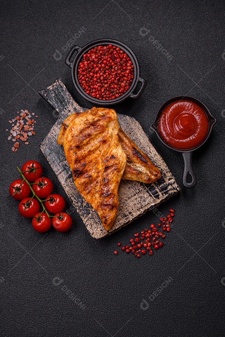 Delicioso filé de frango grelhado fresco com especiarias e ervas em um fundo escuro de concreto. Um prato cozido no fogo
