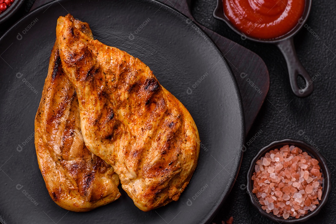 Delicioso filé de frango grelhado fresco com especiarias e ervas em um fundo escuro de concreto. Um prato cozido no fogo