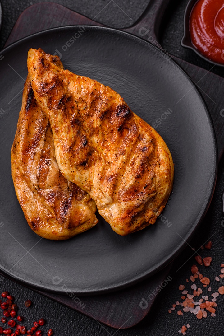 Delicioso filé de frango grelhado fresco com especiarias e ervas em um fundo escuro de concreto. Um prato cozido no fogo