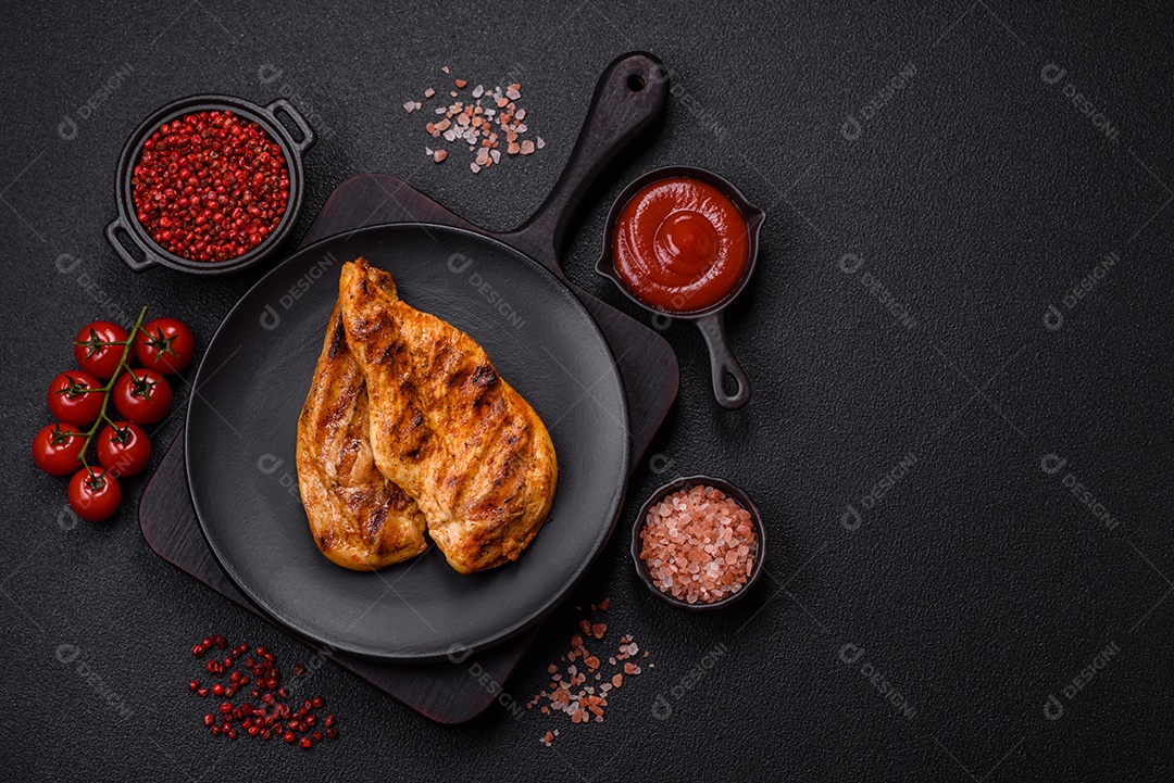 Delicioso filé de frango grelhado fresco com especiarias e ervas em um fundo escuro de concreto. Um prato cozido no fogo